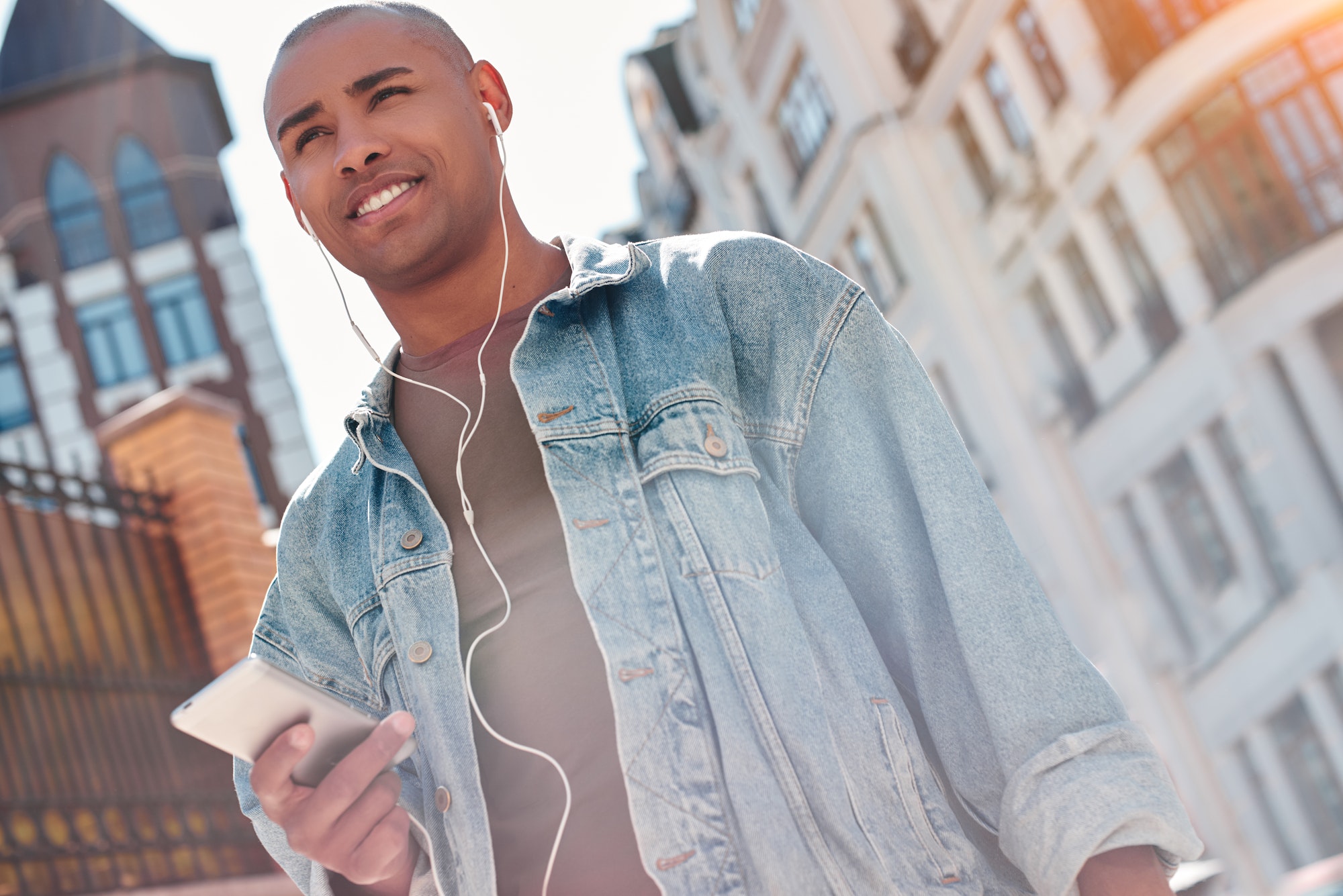 Music lover. Young guy wearing earphones walking on city street listening to music holding