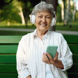 Old woman in headphones listens to music on bench